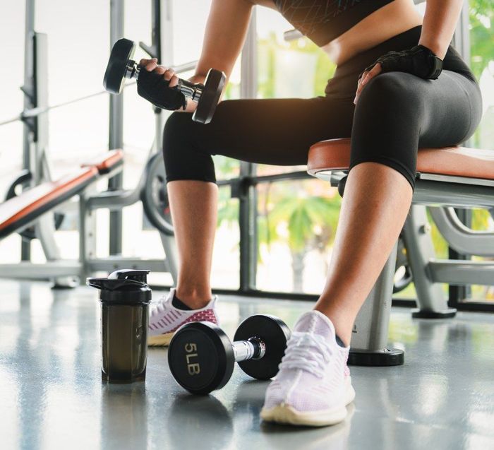  woman is sitting on a bench in a gym holding a dumbbell.