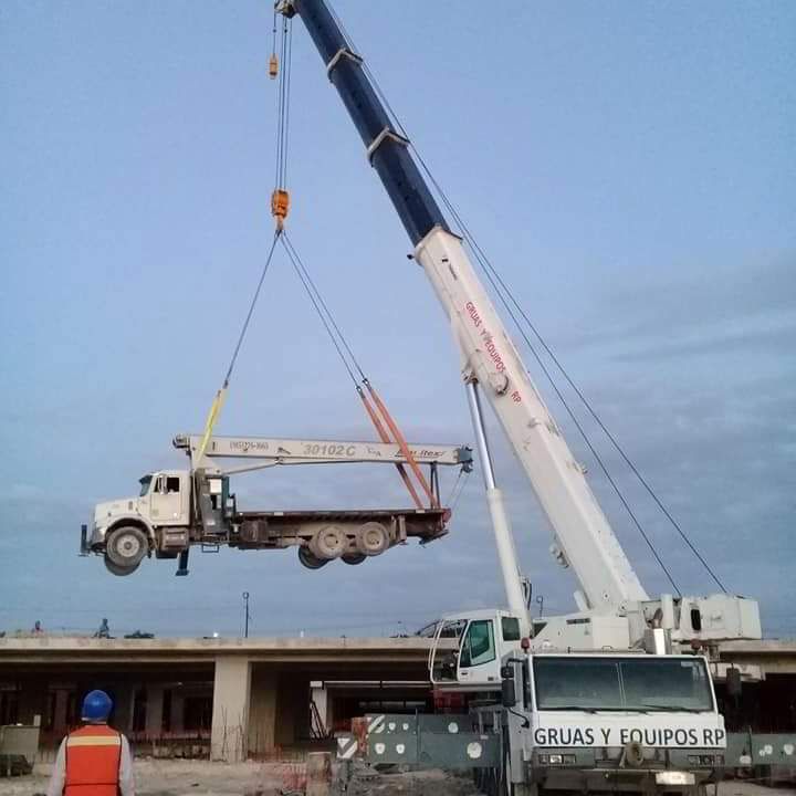 Grúa levantando un camión en un sitio de construcción; cielo azul.
