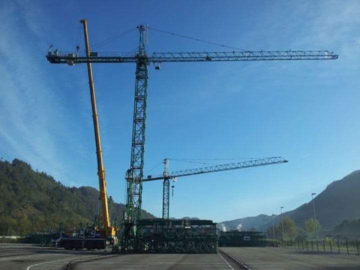 Varias grúas en una obra en construcción, con montañas al fondo bajo un cielo azul.