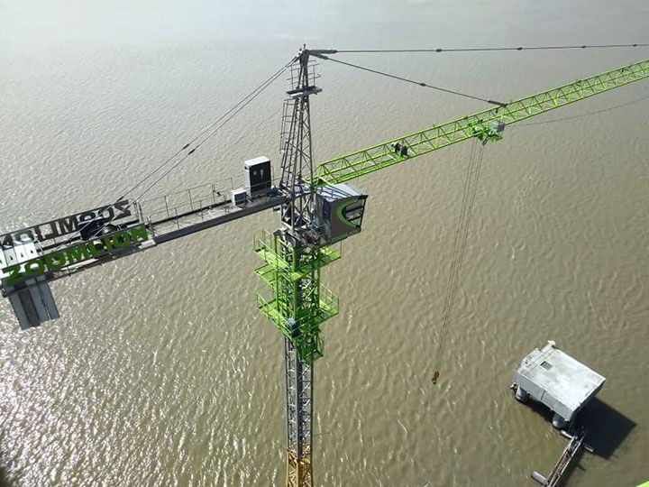 Grúa en zona inundada, verde y gris, con un pequeño edificio cercano.