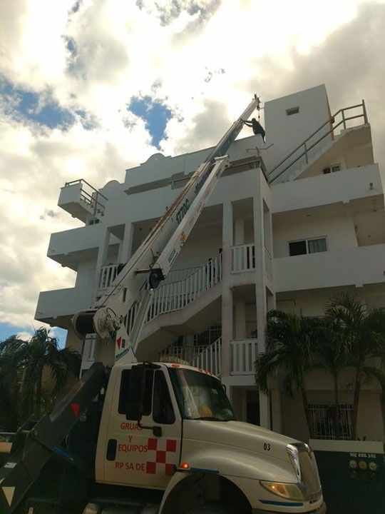Edificio blanco con escalera exterior; camión con ascensor que sube a la cima. Cielo nublado.