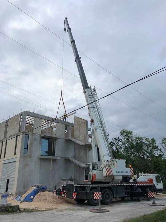Sitio de construcción: una grúa levanta una viga de hormigón hasta el segundo piso de un edificio, cielo nublado arriba.