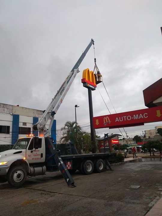 Una grúa levanta un cartel de McDonald's con arcos dorados, cerca de un drive-thru, en un día nublado.