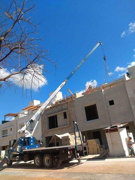 Grúa elevando materiales a un edificio en construcción en un día soleado.