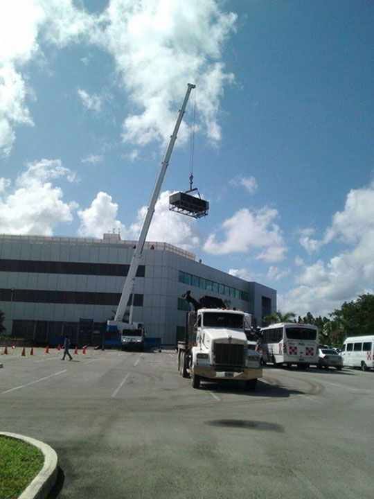 Una grúa levanta un vehículo delante de un edificio; debajo hay un camión y autobuses aparcados.