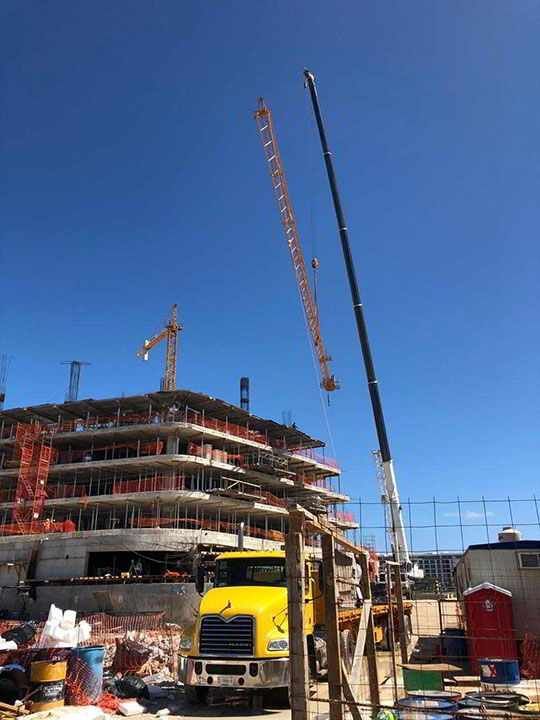 Sitio de construcción con camión amarillo, grúa y edificio de varios pisos en construcción contra un cielo azul claro.