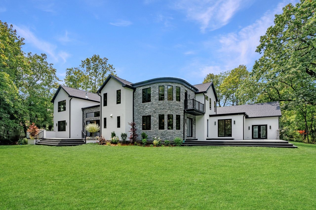 A large house is sitting on top of a lush green lawn surrounded by trees.