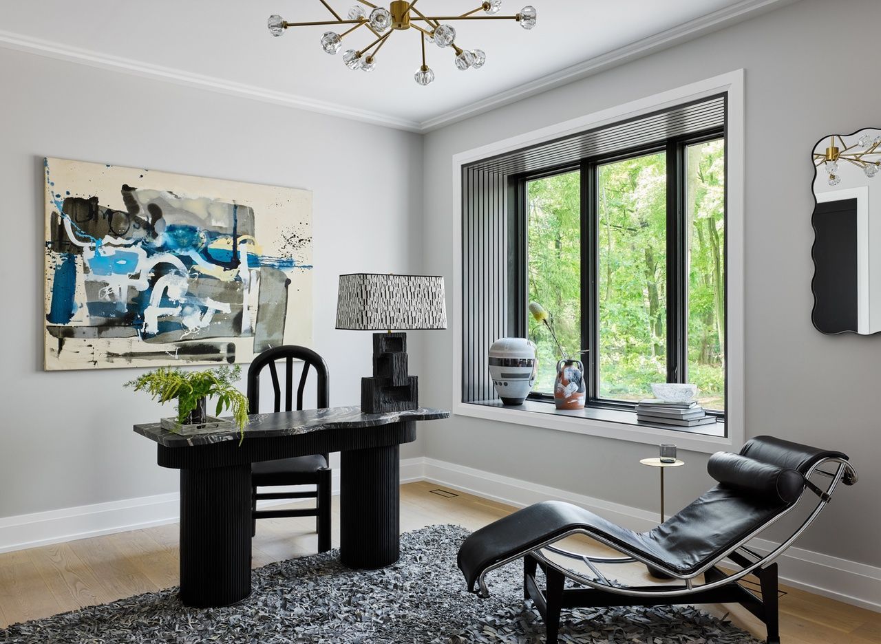 A living room with a desk , chair , chaise lounge and a large window.