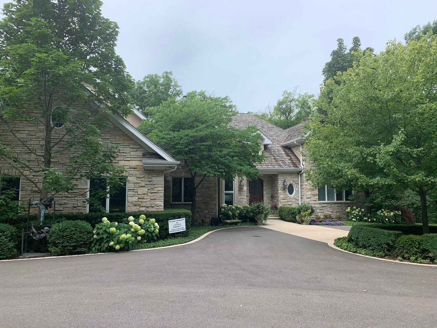 A large house with a driveway leading to it is surrounded by trees and bushes.