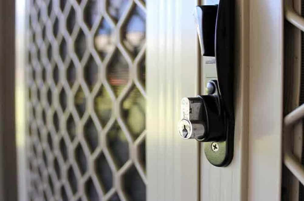 A close-up view of a metal security screen door handle and key lock mechanism mounted on a cream-colored frame.