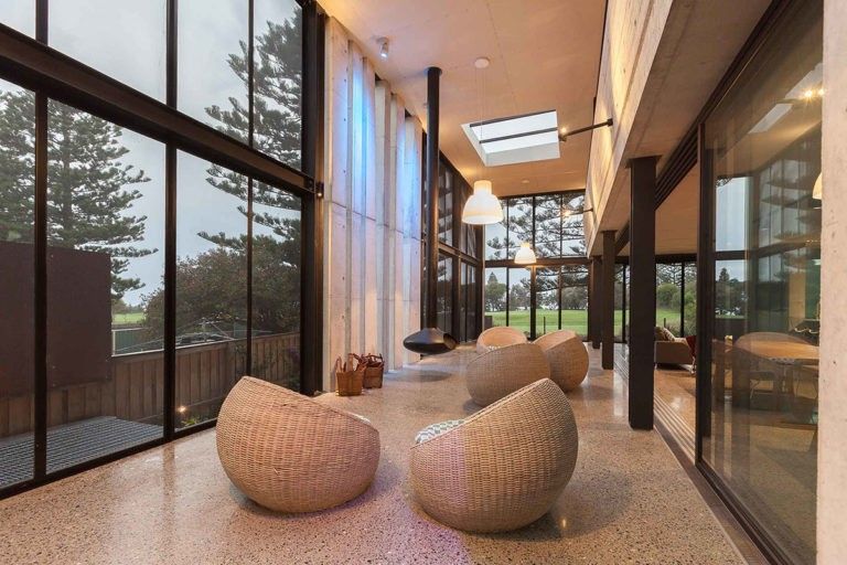 Modern lounge with woven chairs, terrazzo floor, and floor-to-ceiling windows in a bright corridor.