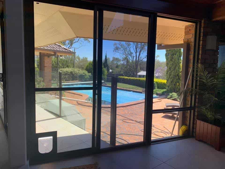 A sliding glass door with a pet door installed at the bottom, looking out onto a backyard swimming pool and patio.
