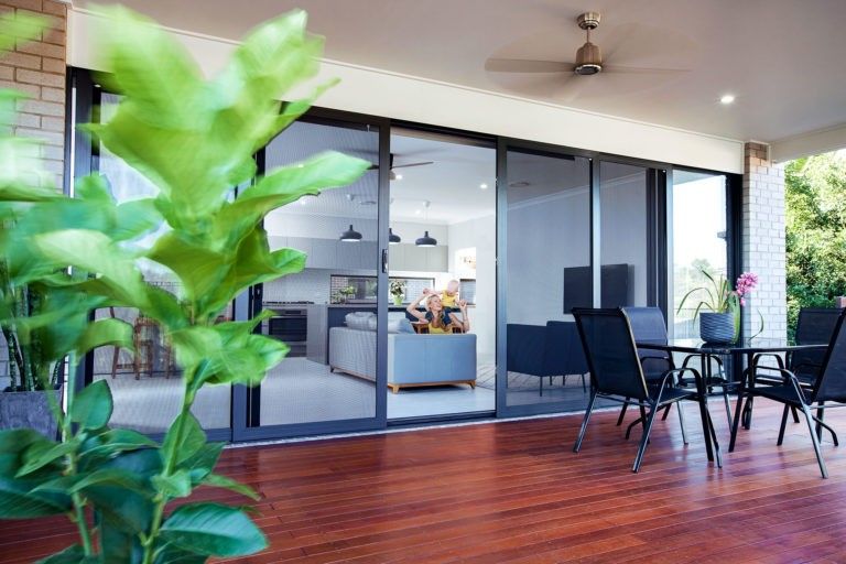 Covered patio with wooden deck, black outdoor furniture, and sliding glass doors overlooking a modern interior