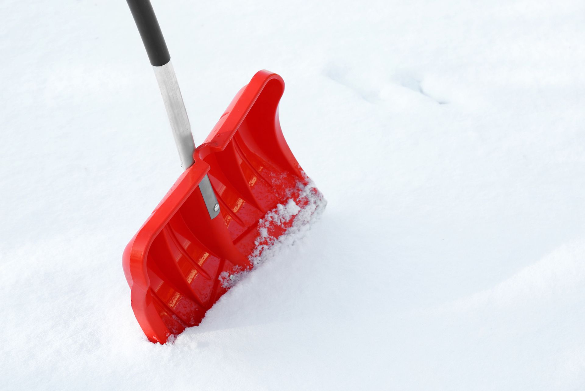 Red snow shovel stuck in fresh white snow.