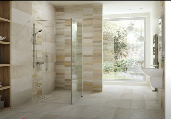 Modern bathroom with glass shower, neutral tile walls, large window overlooking greenery.