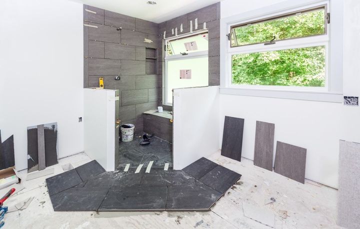 Bathroom under construction with gray tile, white walls, and a window.