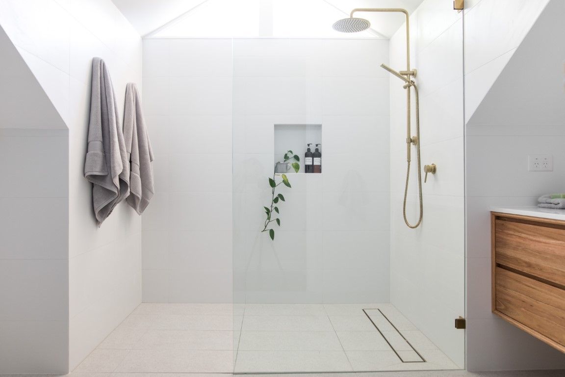 Modern white bathroom with a glass shower, gold fixtures, and wooden vanity.