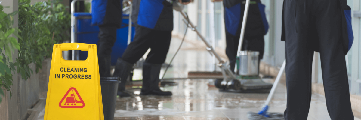 Cleaning in progress sign in focus with cleaning crew moping and polishing floors in blurred background