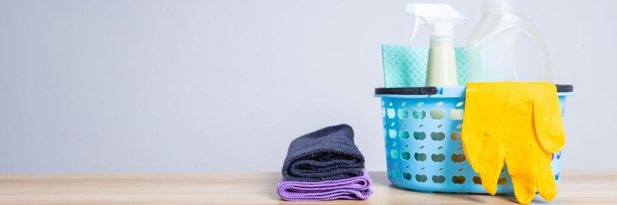 A basket filled with cleaning supplies and gloves on a wooden table.
