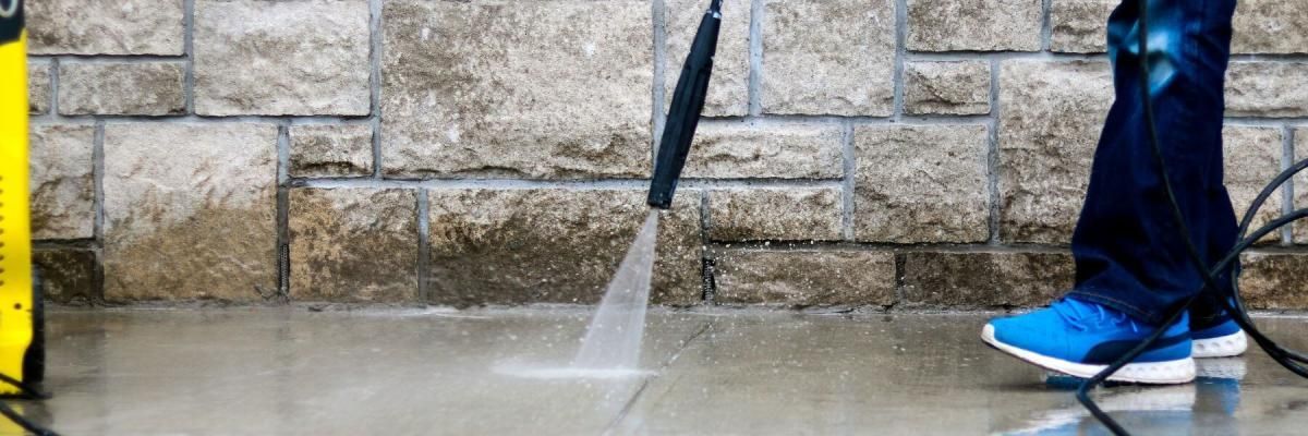 A person is using a high pressure washer to clean a brick wall.