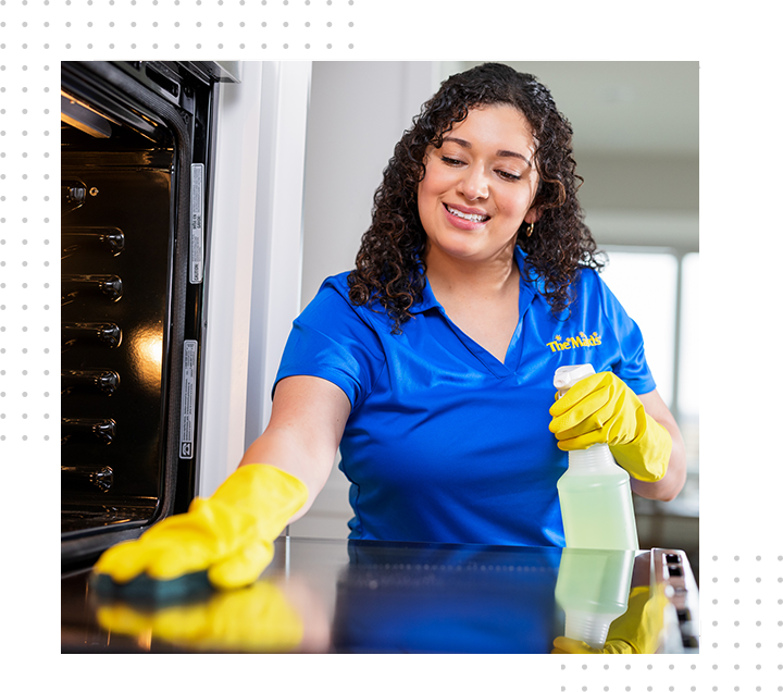 Person in blue shirt and yellow gloves cleaning an oven with a spray bottle in a kitchen