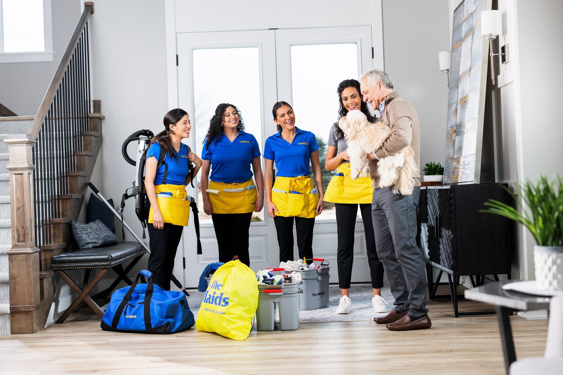 Four cleaners with yellow buckets standing in a bright room with cleaning supplies on the floor