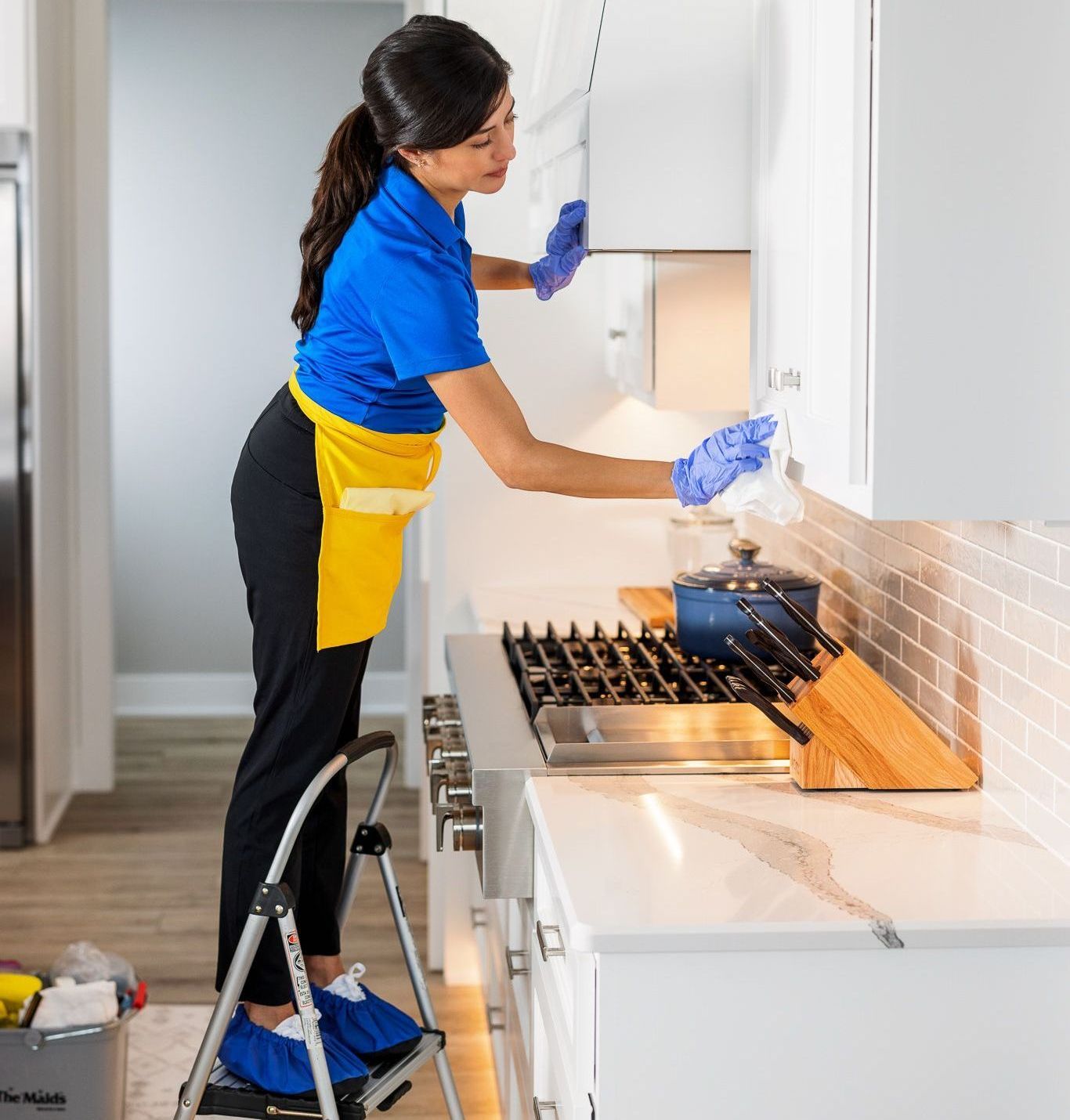 Person cleaning white kitchen cabinets and stove in a bright kitchen.