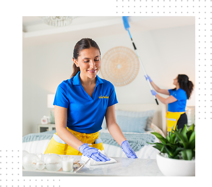 Woman in blue uniform cleaning a bright room with another worker in the background