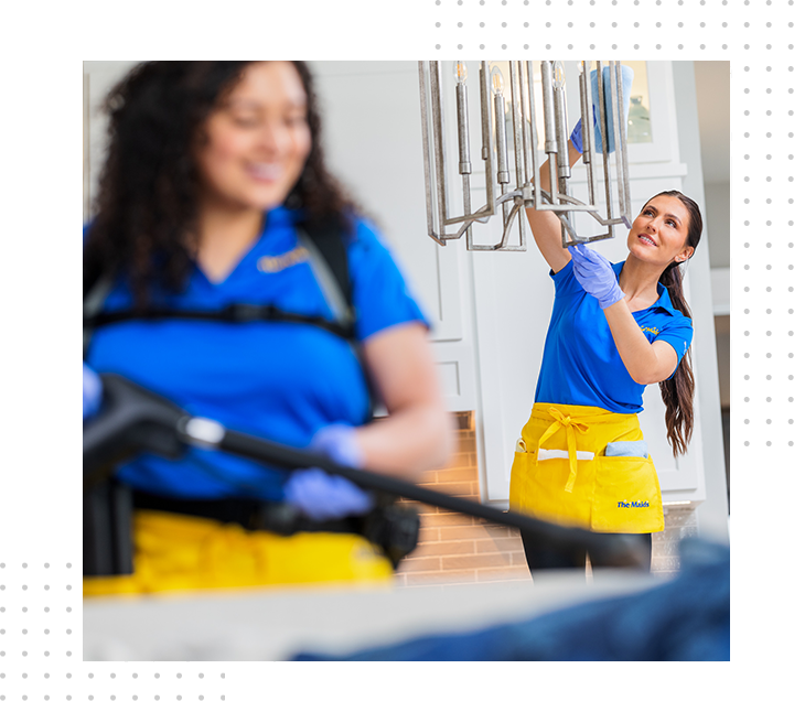 Two cleaners in blue shirts and yellow aprons polish hanging glass fixtures in a bright lobby