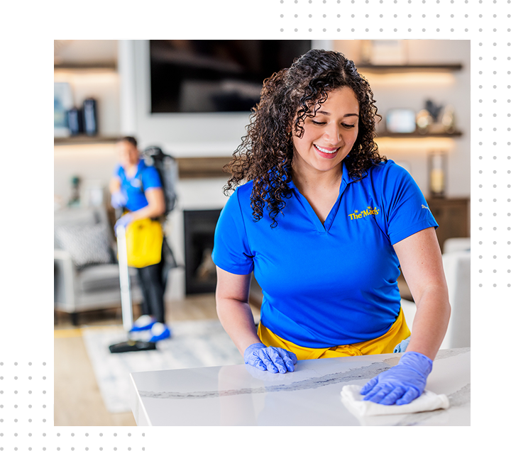 Woman in blue shirt and gloves wiping a countertop in a bright kitchen
