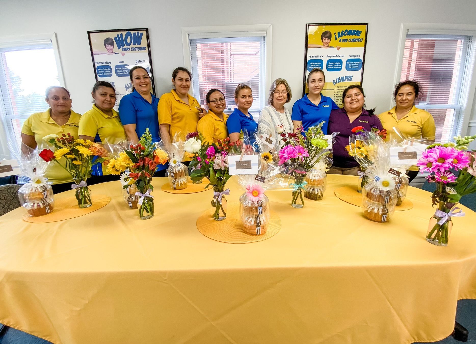 Group of people in yellow shirts posing behind a decorated table with flowers and drinks indoors
