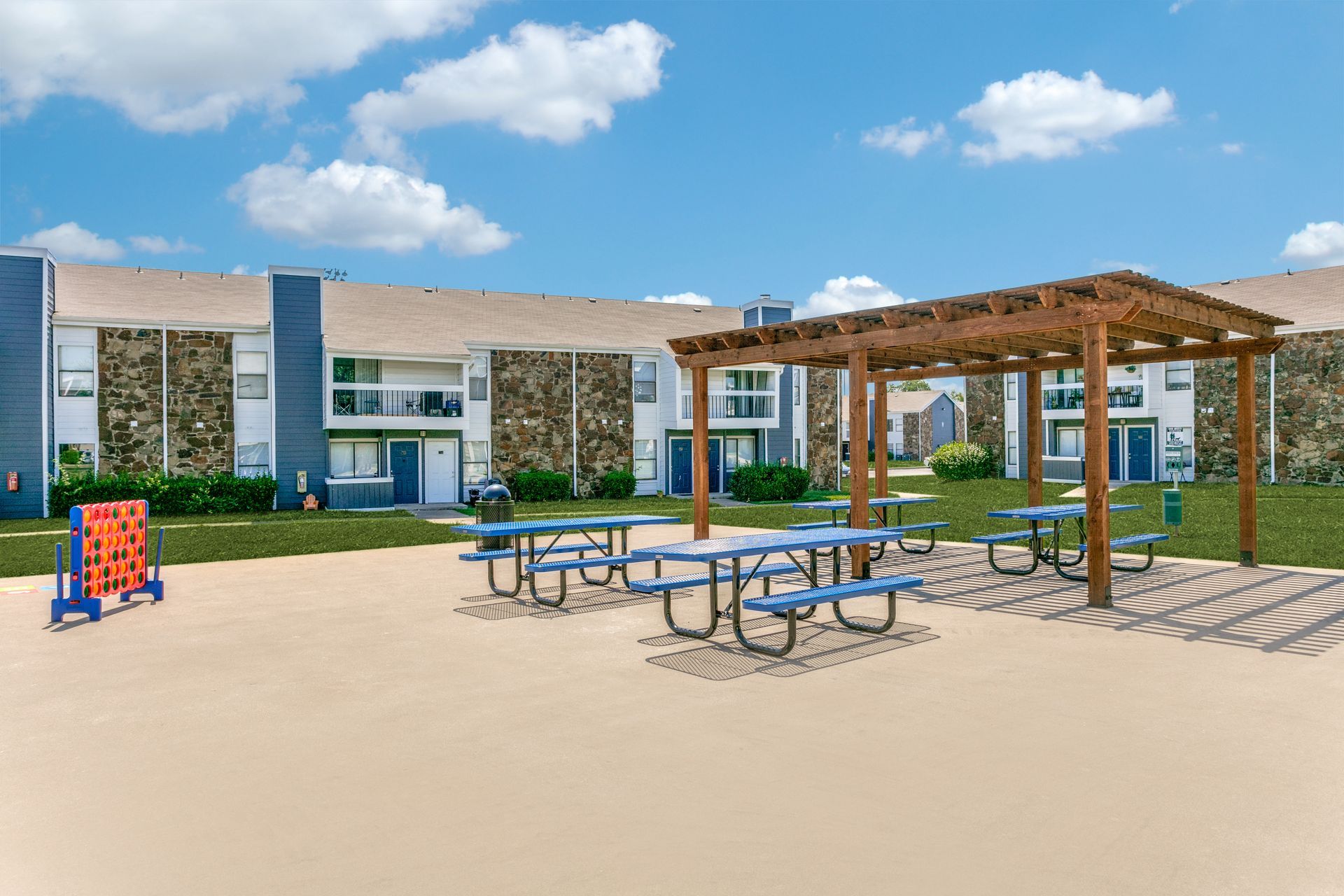 Outdoor recreation area with picnic tables, pergola, and apartment building in the background.