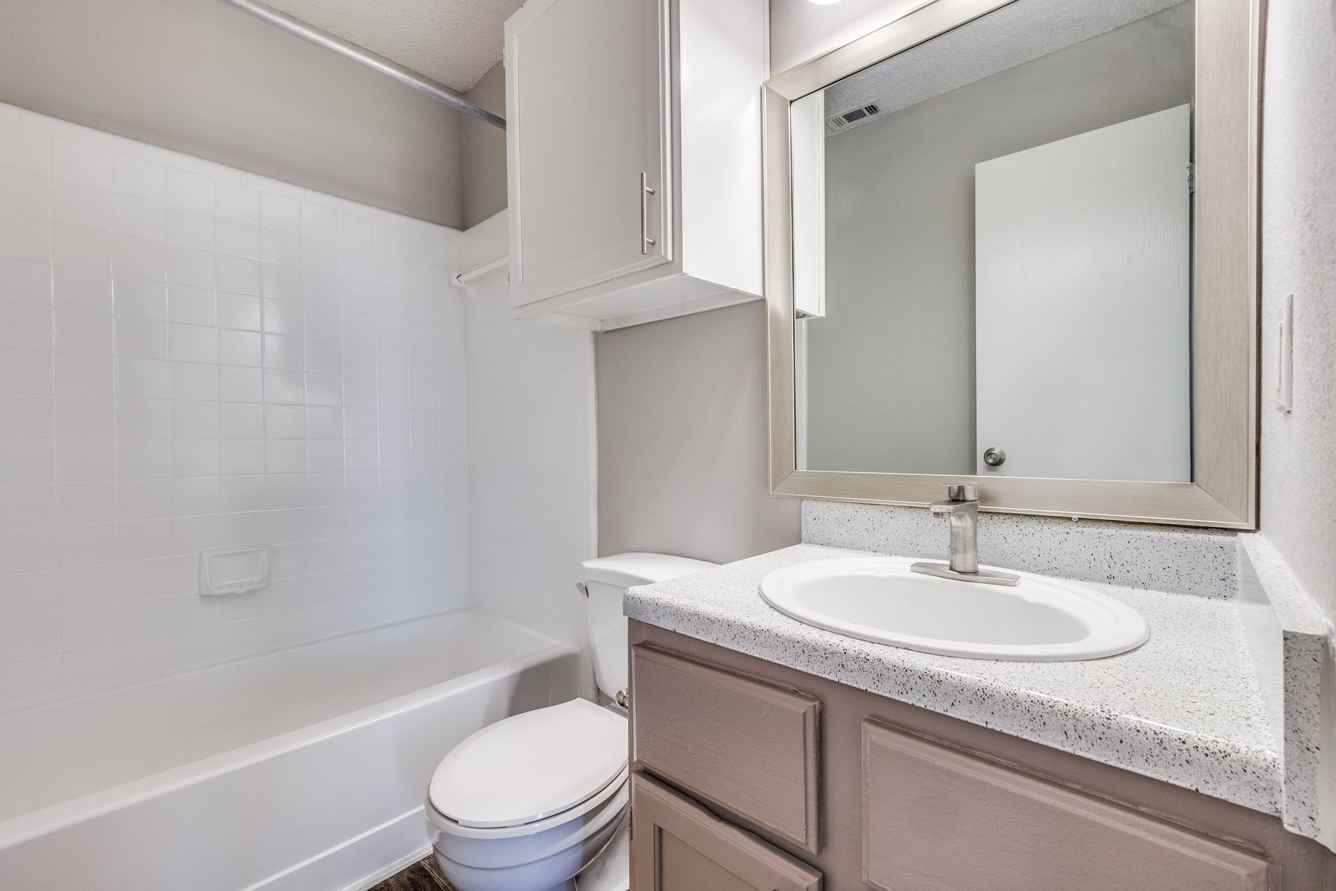 Bathroom with white tub, toilet, vanity with sink, mirror, and cabinet. Gray walls.