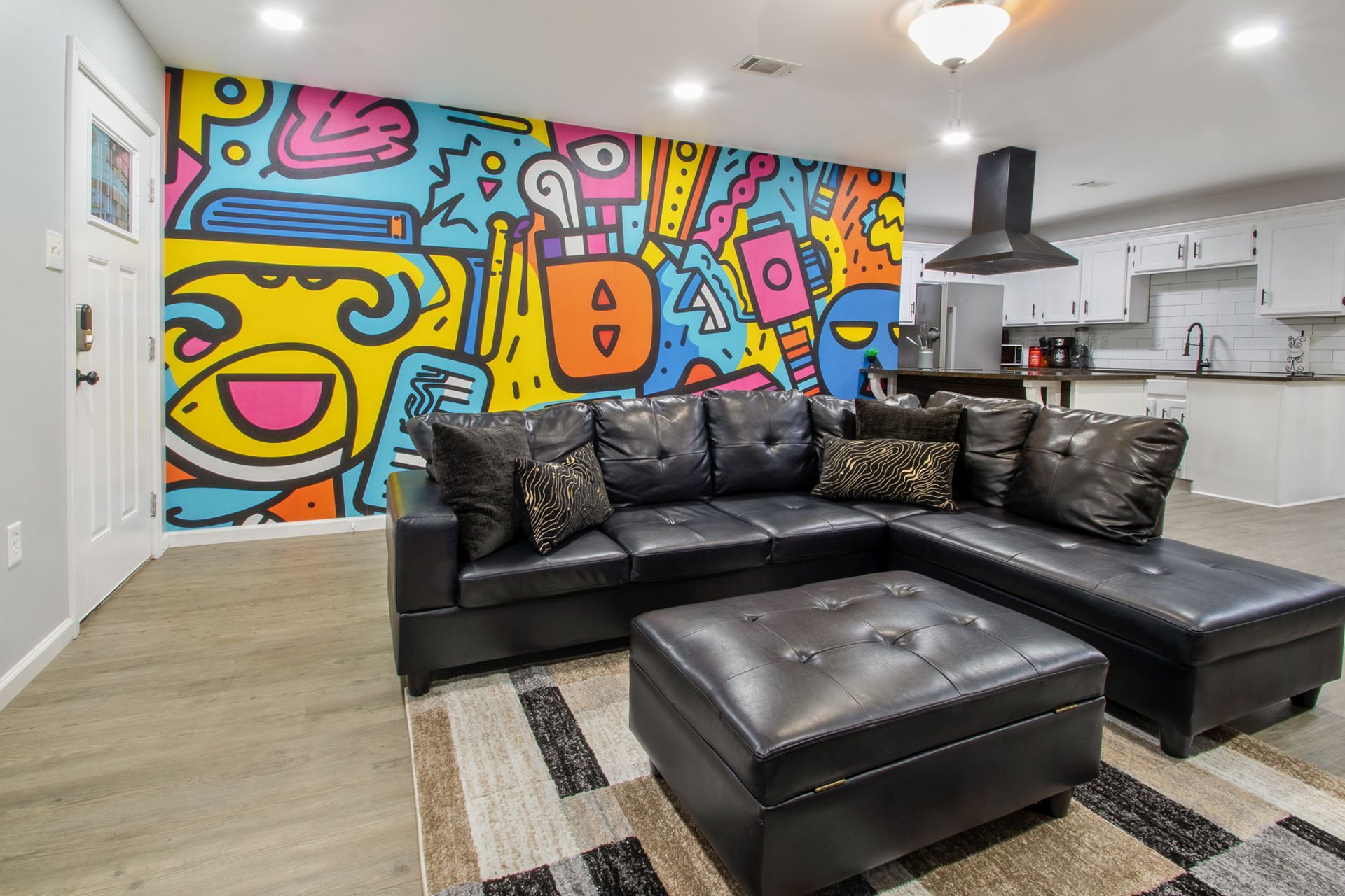 A living room with a couch and ottoman and a colorful mural on the wall.