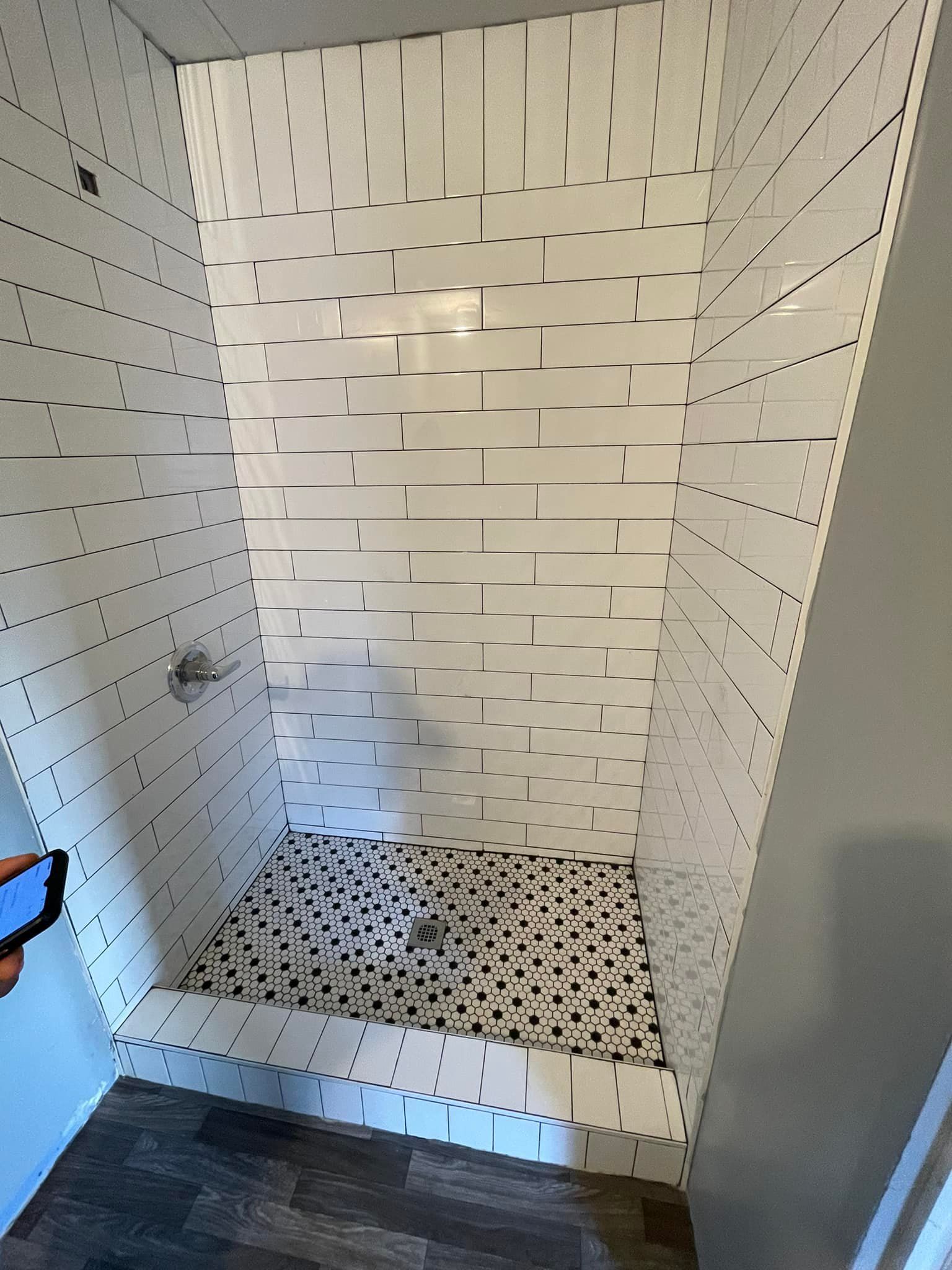 A person is taking a picture of a shower with white tiles.