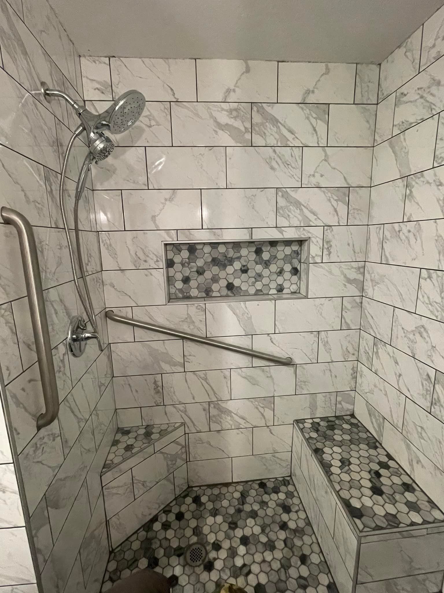 A shower with a stainless steel railing and a bench.