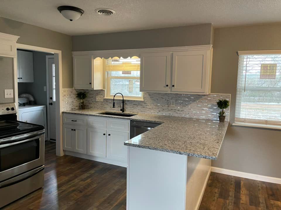 A kitchen with white cabinets , granite counter tops , a stove and a sink.