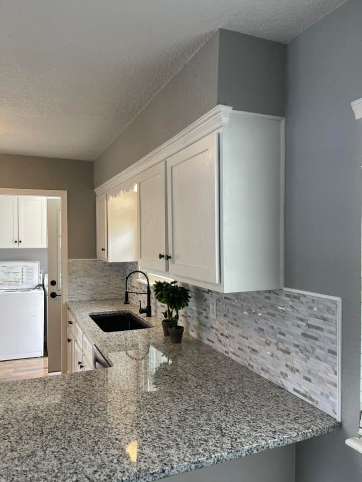 A kitchen with granite counter tops , white cabinets , a sink , and a window.