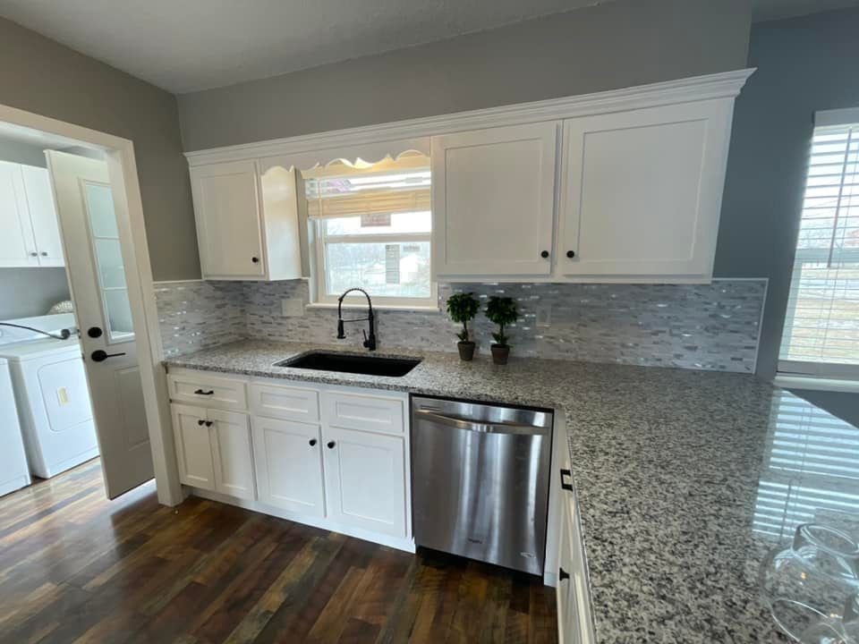 A kitchen with white cabinets , granite counter tops , a sink and a stainless steel dishwasher.