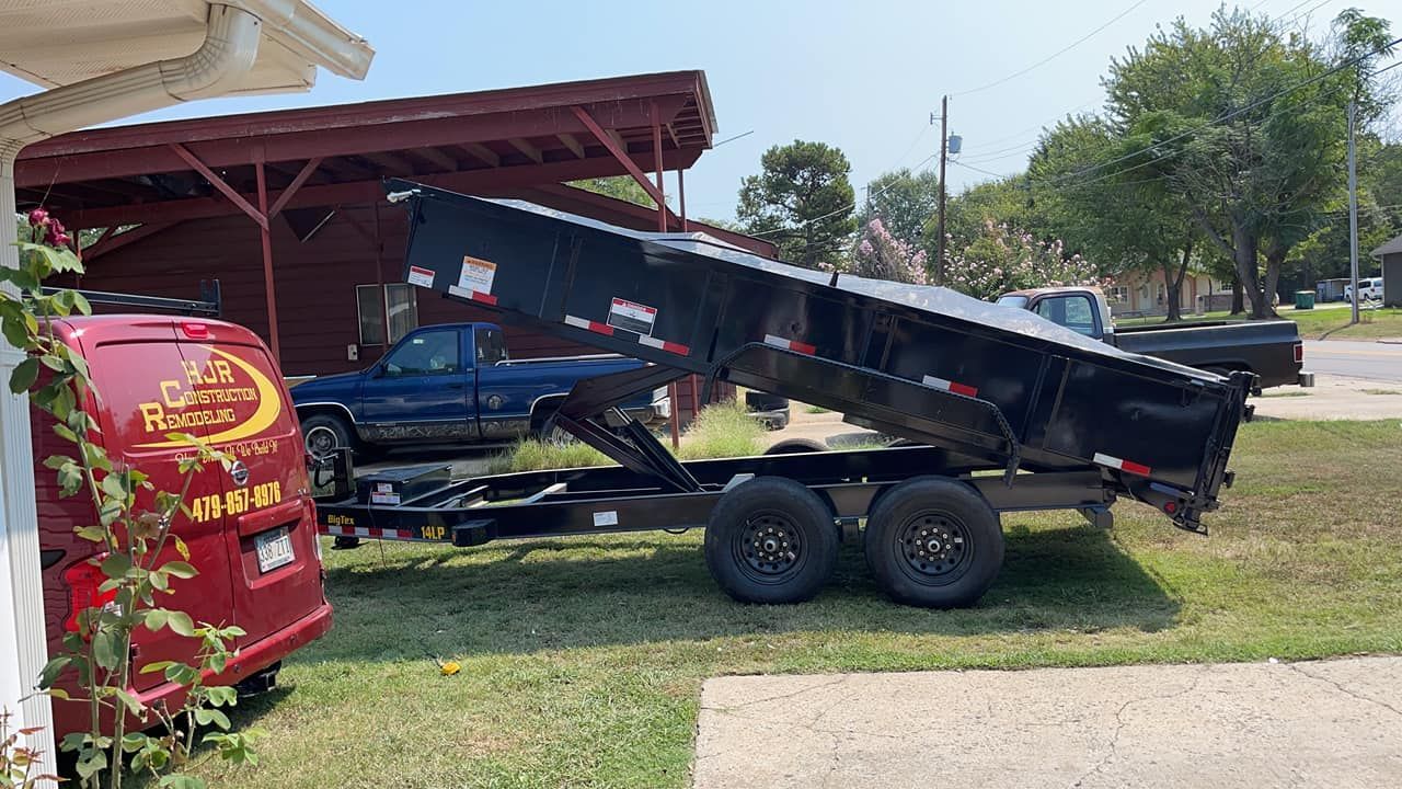 A dump truck is being towed by a trailer in a yard.