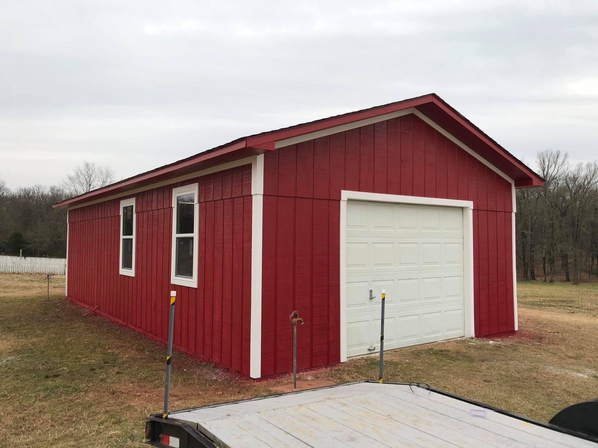 A red garage with a white garage door and a trailer parked in front of it.