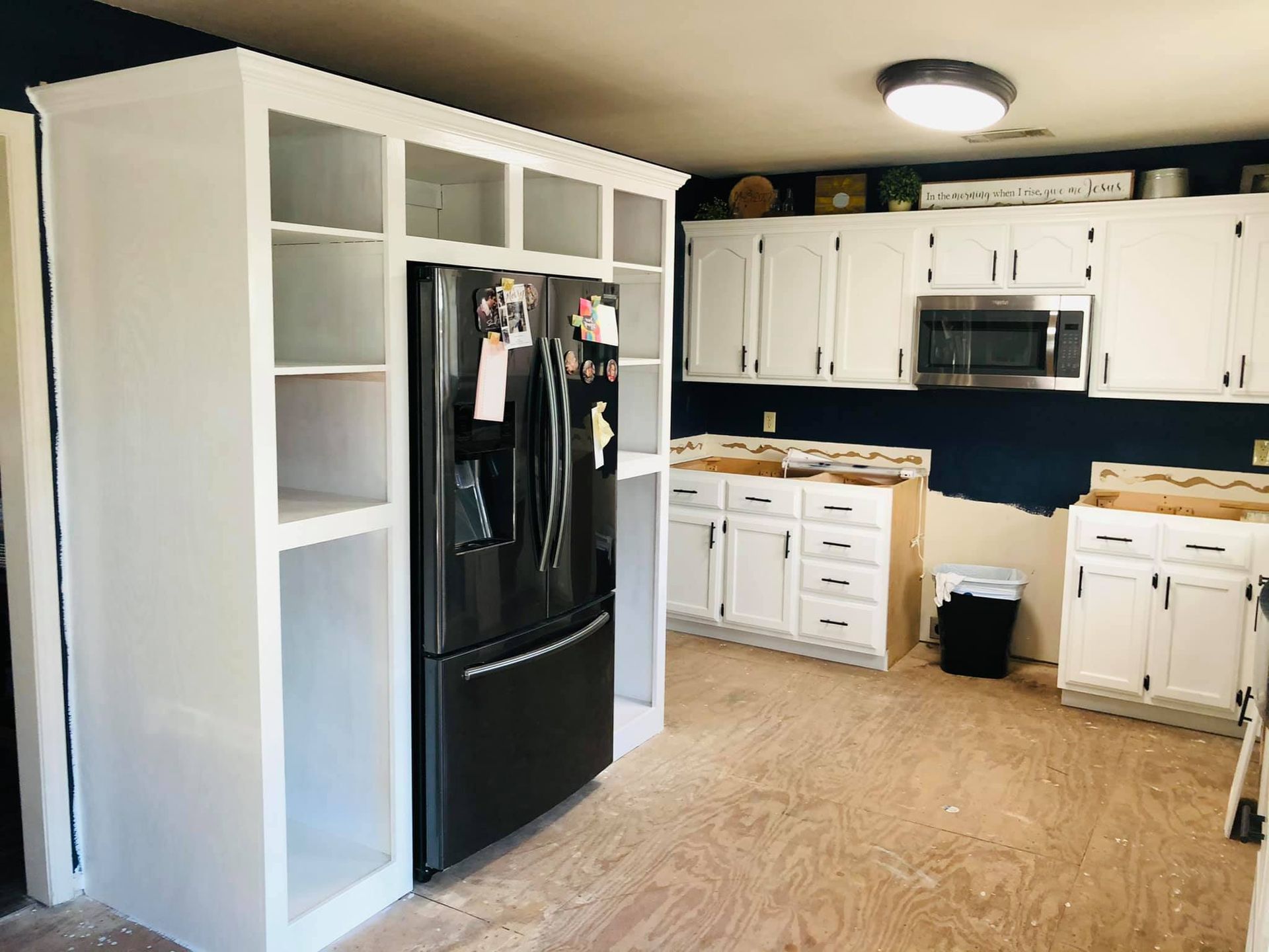 A kitchen with white cabinets and a black refrigerator.