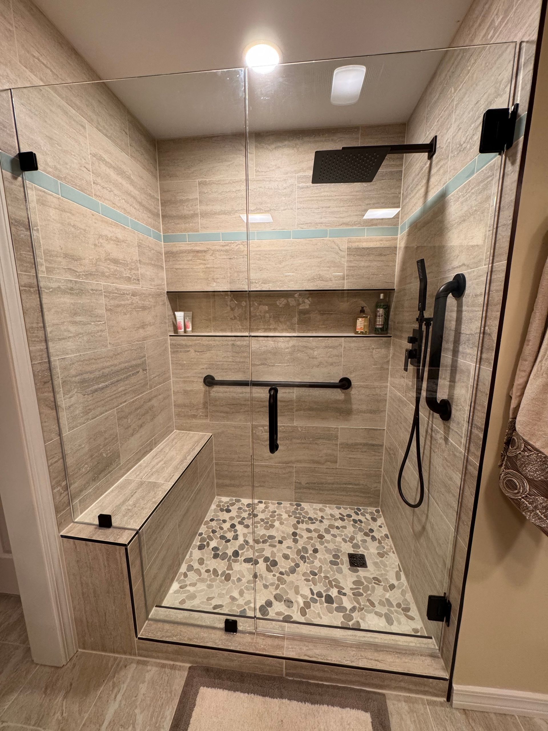 A bathroom with a walk in shower with a glass door and a bench.
