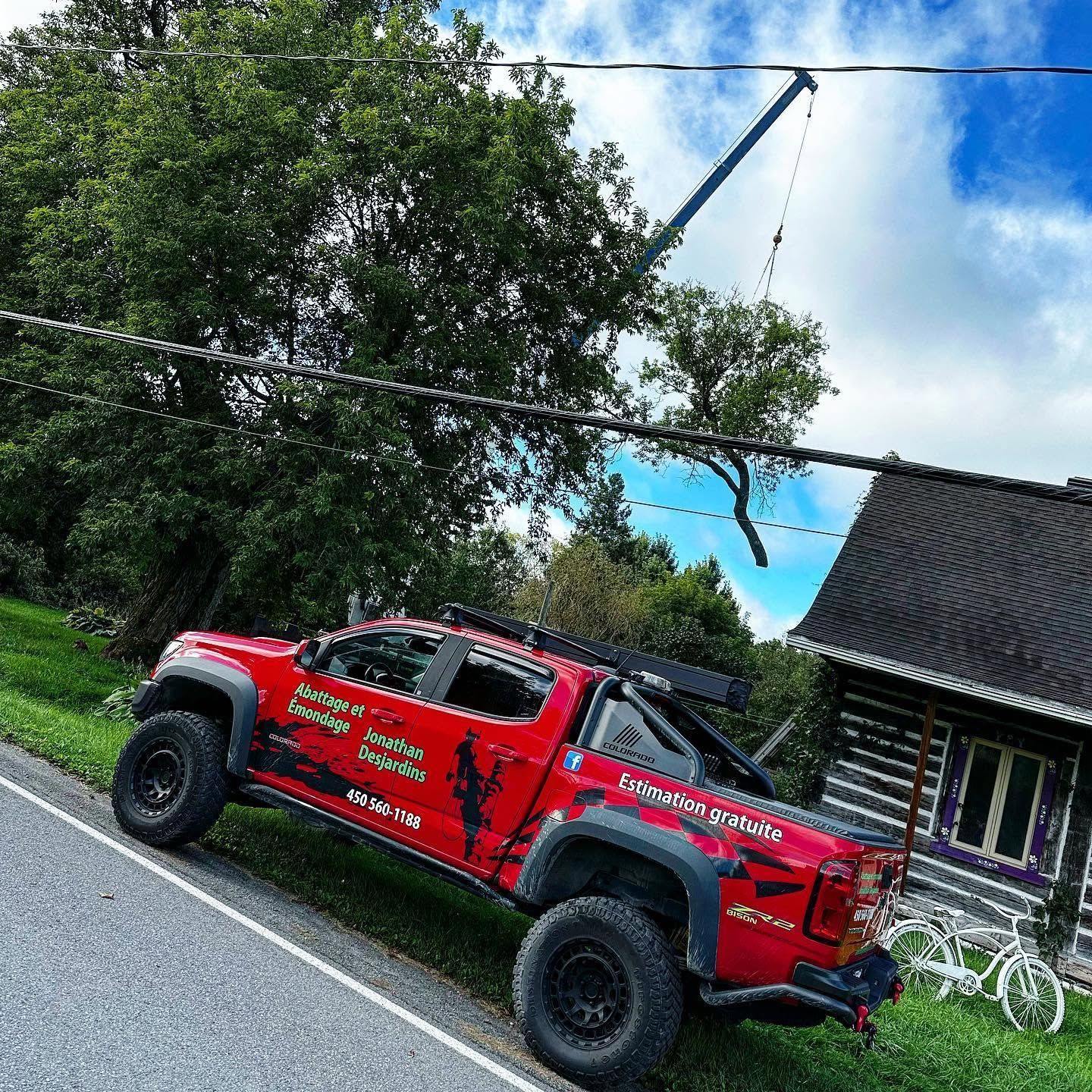 Un pick-up rouge tout-terrain garé au bord de la route, à côté d’une maison, avec des arbres et un ciel bleu éclatant.