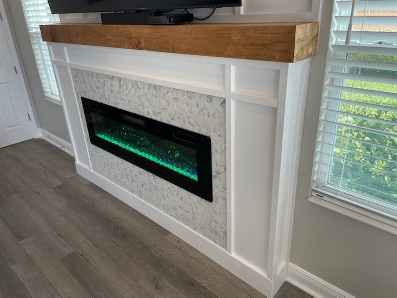 Electric fireplace with white surround, marble tile, and wood mantel below a TV.