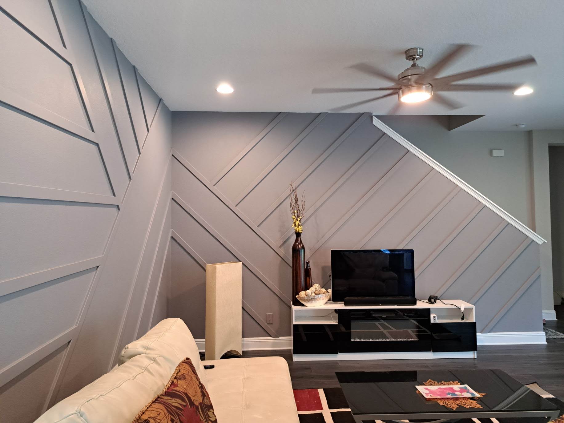 Gray accent wall with angled trim in a living room. TV, console, and beige couch visible.