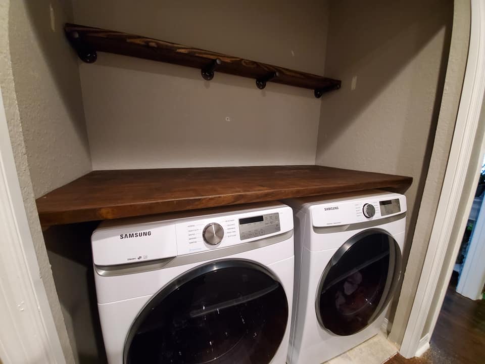 Laundry room with a wooden countertop over a white washer and dryer. A shelf with hooks is above.