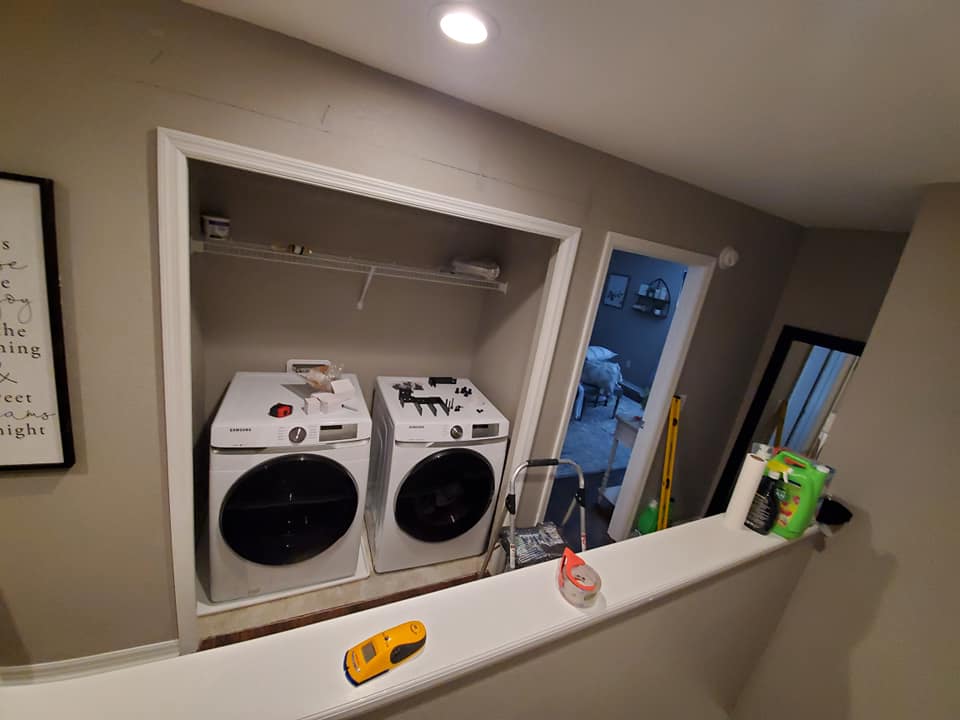 Laundry machines in a recessed wall, with open door and railing in foreground.