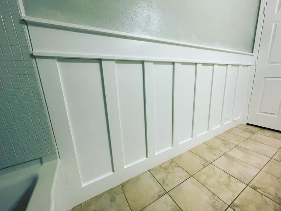 White wainscoting on a bathroom wall, with a tiled floor and door visible.