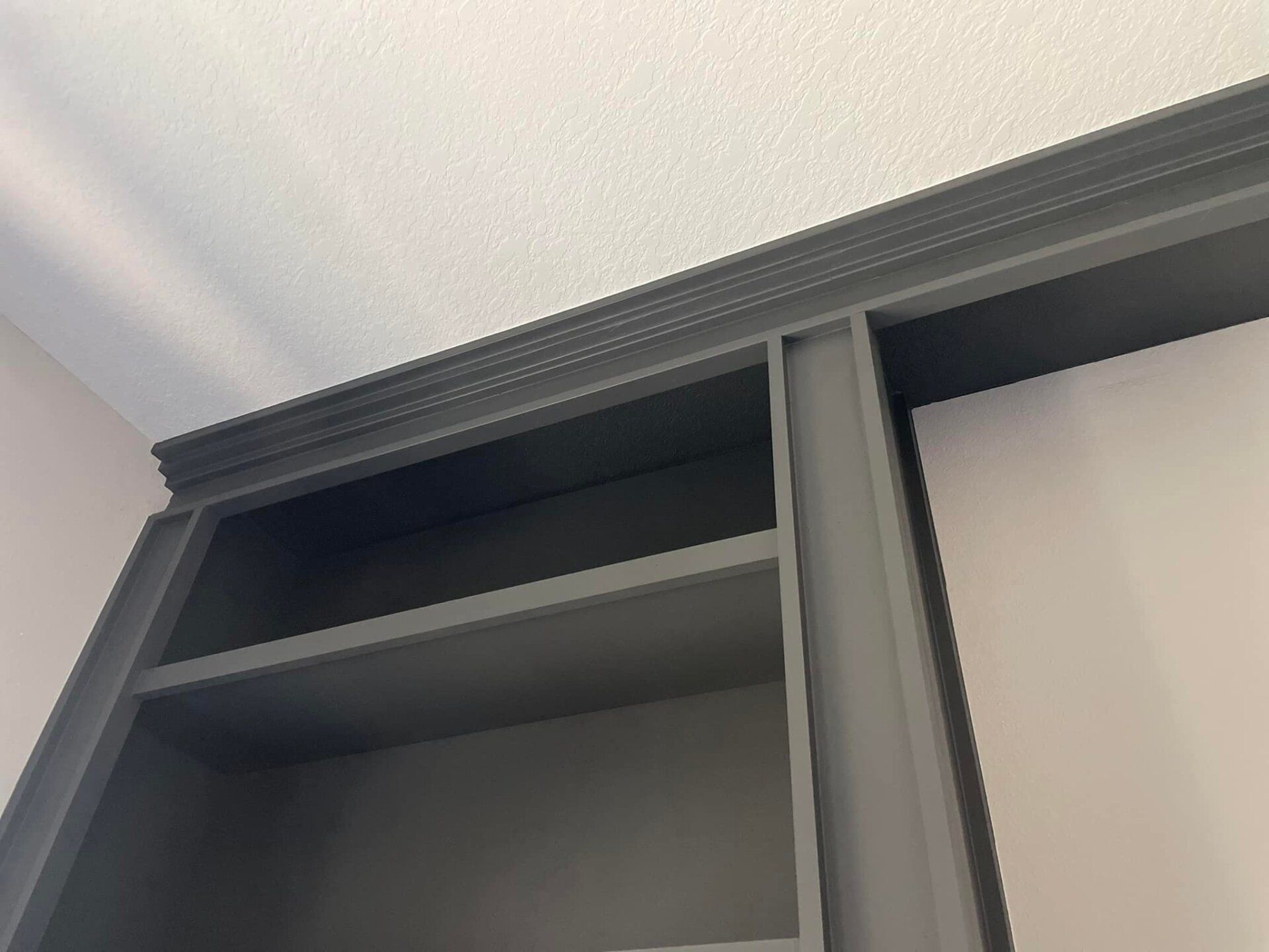 Gray built-in shelving unit against a white ceiling and wall, with a decorative crown molding detail.